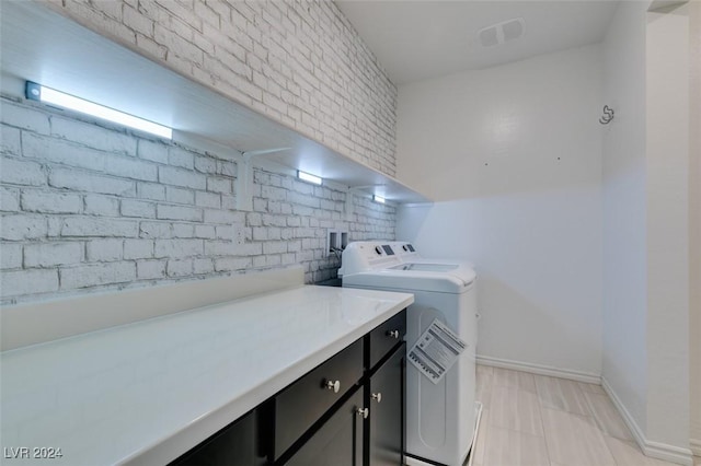 washroom featuring cabinets, brick wall, and washer and clothes dryer