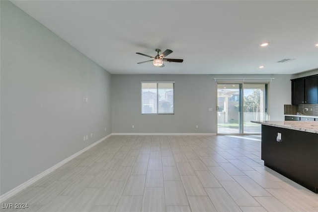 kitchen with ceiling fan, a wealth of natural light, decorative backsplash, and light stone countertops