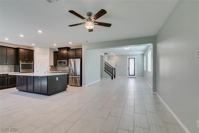 kitchen featuring tasteful backsplash, ceiling fan, a center island with sink, dark brown cabinetry, and stainless steel appliances