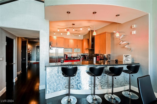 kitchen featuring wall chimney range hood, kitchen peninsula, stainless steel fridge, dark wood-type flooring, and decorative light fixtures