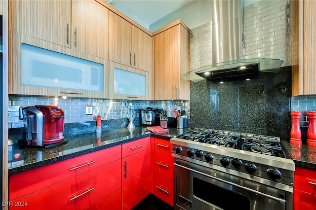 kitchen with wall chimney range hood, stainless steel stove, dark stone counters, and backsplash