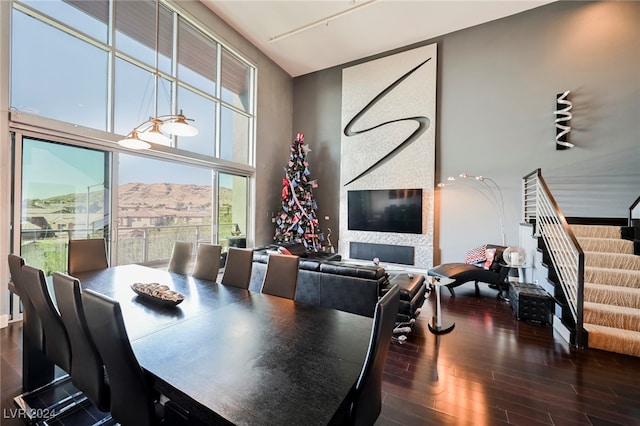 dining space with a large fireplace, a towering ceiling, and dark hardwood / wood-style flooring