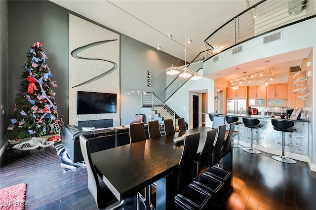 dining area featuring a large fireplace, dark wood-type flooring, and a high ceiling