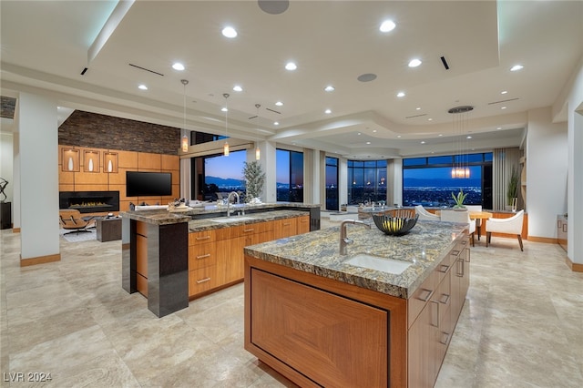 kitchen with a large island, sink, hanging light fixtures, and light stone counters