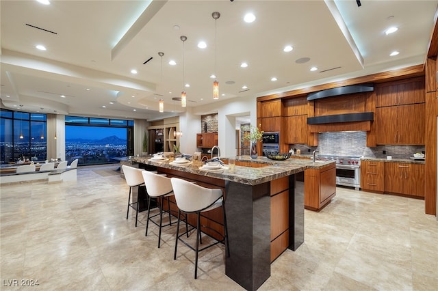 kitchen with a large island with sink, high end stainless steel range oven, a kitchen bar, light stone counters, and tasteful backsplash