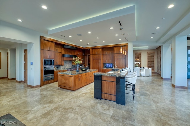 kitchen featuring light stone countertops, appliances with stainless steel finishes, backsplash, a breakfast bar area, and a center island with sink