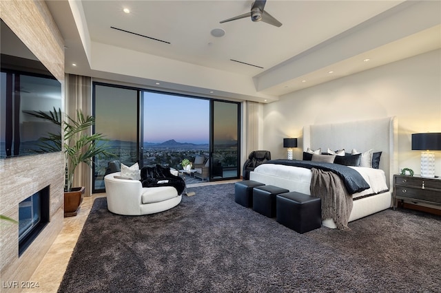 bedroom featuring access to outside, a fireplace, ceiling fan, light carpet, and a wall of windows