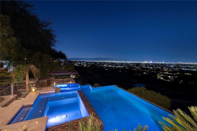 pool at twilight with a pool with connected hot tub and a patio