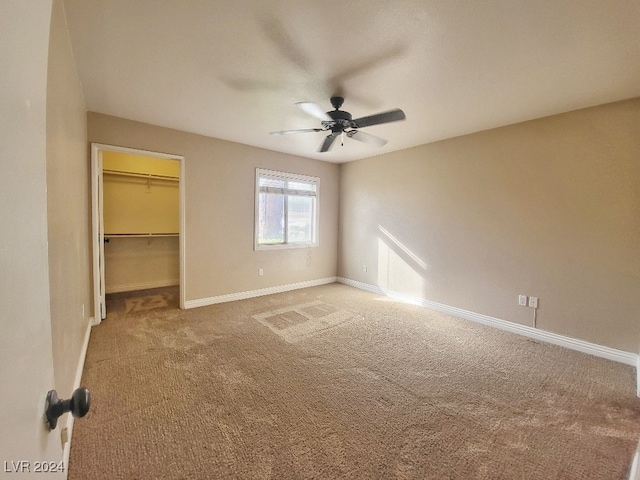 unfurnished bedroom with carpet, a walk in closet, a closet, and ceiling fan