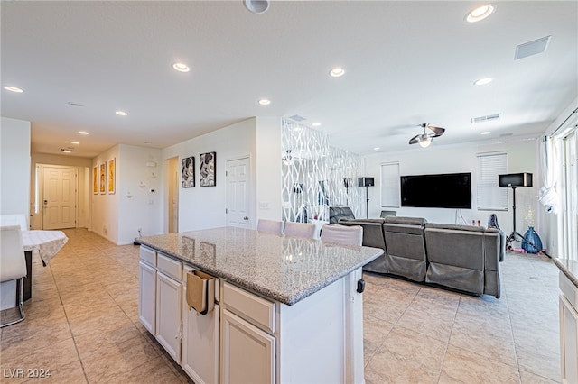 kitchen with a kitchen island, white cabinetry, light stone counters, and ceiling fan