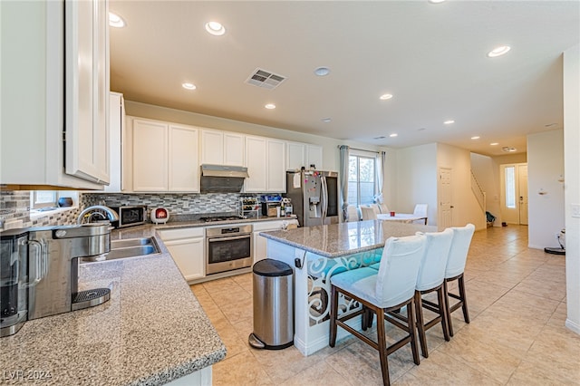 kitchen featuring a breakfast bar area, white cabinetry, stainless steel appliances, sink, and a center island