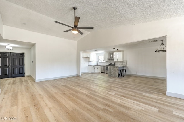 unfurnished living room with a textured ceiling, vaulted ceiling, light wood-type flooring, and ceiling fan with notable chandelier