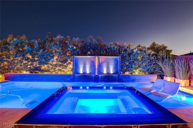 pool at twilight featuring an in ground hot tub