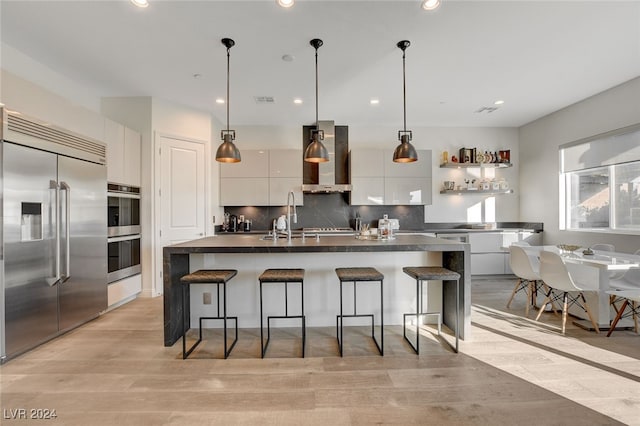 kitchen featuring stainless steel appliances, hanging light fixtures, an island with sink, and white cabinets