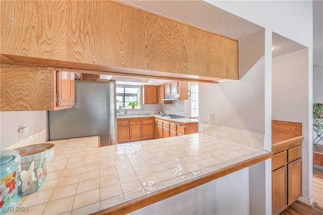 kitchen featuring tile countertops, kitchen peninsula, stainless steel appliances, and light hardwood / wood-style floors