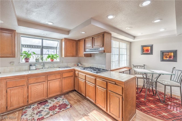 kitchen featuring stainless steel gas cooktop, a raised ceiling, sink, and light wood-type flooring