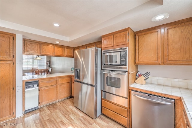 kitchen featuring a textured ceiling, appliances with stainless steel finishes, tile counters, and light wood-type flooring