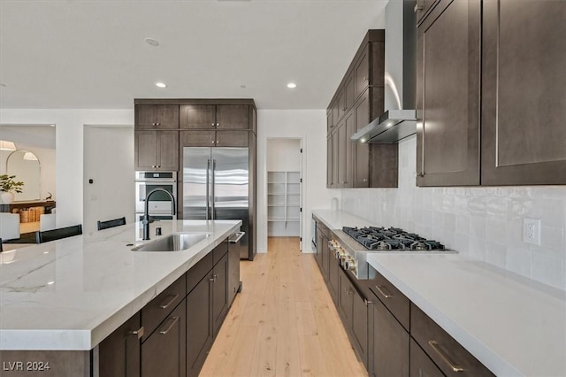 kitchen with backsplash, wall chimney range hood, sink, light hardwood / wood-style flooring, and stainless steel appliances