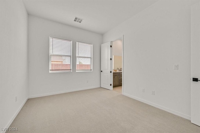 unfurnished bedroom featuring ensuite bathroom and light colored carpet