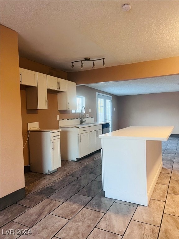 kitchen with a textured ceiling, a center island, white cabinetry, and sink