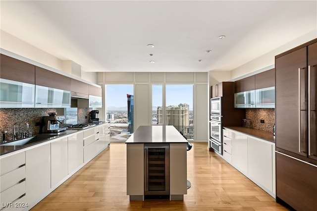 kitchen with a kitchen island, backsplash, wine cooler, white cabinetry, and appliances with stainless steel finishes