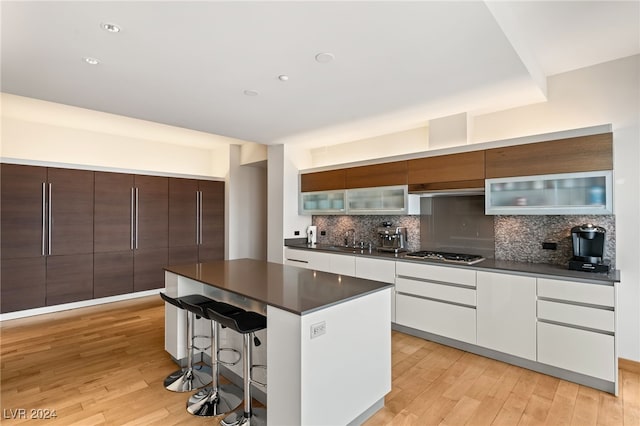 kitchen featuring stainless steel gas cooktop, sink, a center island, white cabinets, and light hardwood / wood-style floors