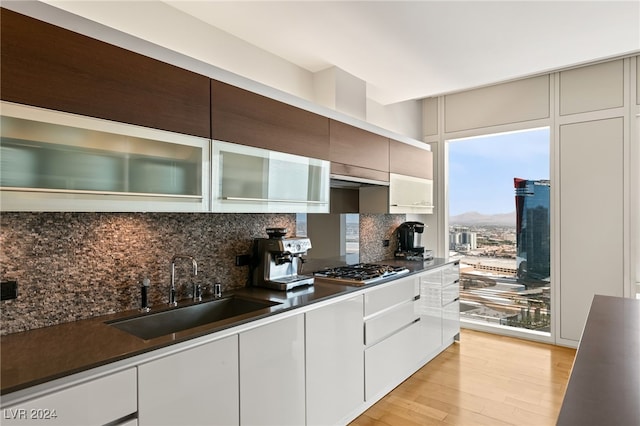 kitchen with stainless steel gas stovetop, light hardwood / wood-style flooring, decorative backsplash, and sink