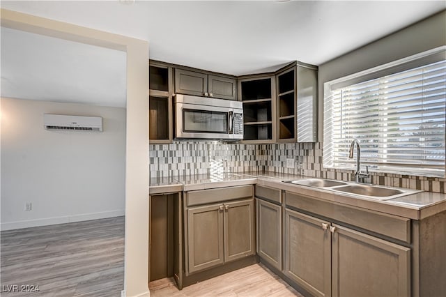 kitchen with an AC wall unit, sink, light hardwood / wood-style flooring, and backsplash