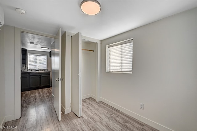 unfurnished bedroom featuring light hardwood / wood-style floors, multiple windows, a closet, and sink