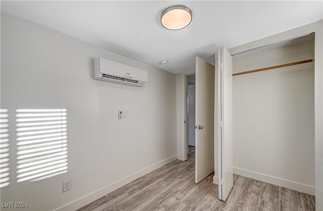 unfurnished bedroom with a closet, a wall mounted AC, and light hardwood / wood-style flooring