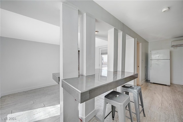 kitchen featuring a breakfast bar area, white fridge, a wall mounted air conditioner, and light hardwood / wood-style floors