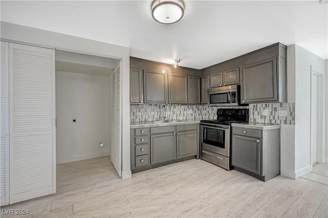 kitchen with light hardwood / wood-style floors, stainless steel appliances, sink, and backsplash