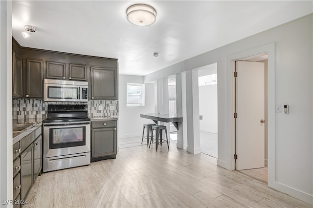 kitchen with backsplash, appliances with stainless steel finishes, dark brown cabinetry, and light wood-type flooring