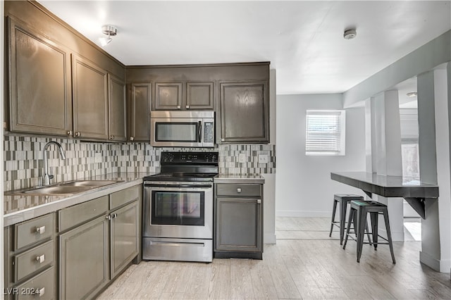 kitchen with appliances with stainless steel finishes, sink, light wood-type flooring, and decorative backsplash