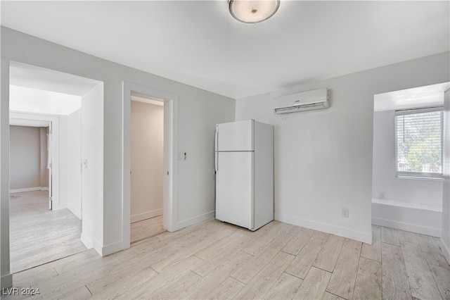 unfurnished bedroom featuring light wood-type flooring, white refrigerator, and a wall unit AC