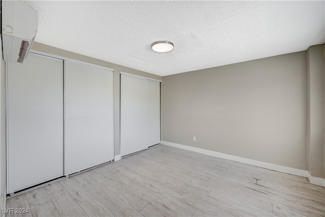 unfurnished bedroom featuring a wall mounted AC, a textured ceiling, and light wood-type flooring