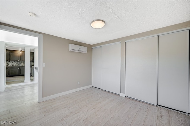 unfurnished bedroom featuring a wall mounted AC, light hardwood / wood-style flooring, and a textured ceiling