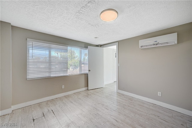 spare room with a textured ceiling, light hardwood / wood-style flooring, and a wall mounted air conditioner