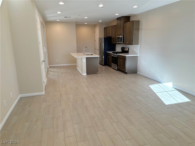 kitchen featuring sink, light wood-type flooring, stainless steel appliances, and a kitchen island with sink