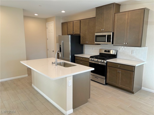 kitchen featuring light wood-type flooring, backsplash, stainless steel appliances, a kitchen island with sink, and sink