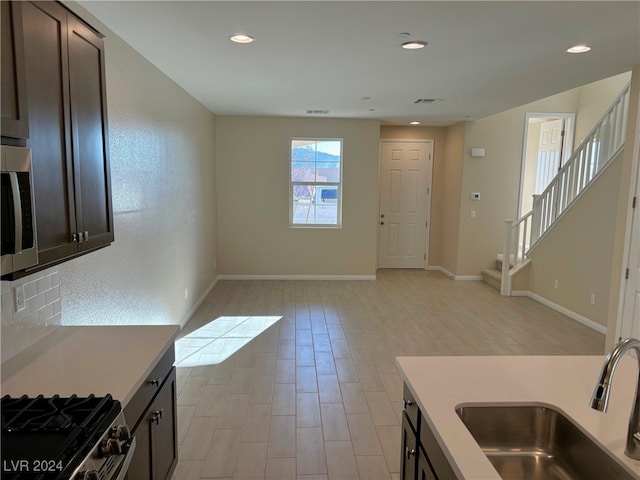 kitchen with sink, stainless steel appliances, backsplash, light hardwood / wood-style floors, and dark brown cabinets