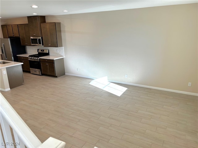 kitchen featuring dark brown cabinetry, stainless steel appliances, light hardwood / wood-style floors, and backsplash