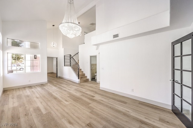 unfurnished living room featuring a towering ceiling, light hardwood / wood-style flooring, and a notable chandelier