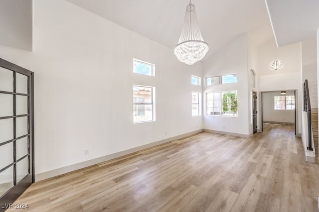 unfurnished living room with a towering ceiling, an inviting chandelier, plenty of natural light, and light wood-type flooring