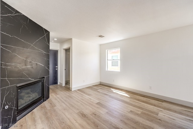 unfurnished living room featuring a fireplace, a textured ceiling, and light wood-type flooring