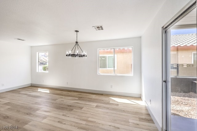 unfurnished dining area with a chandelier, light hardwood / wood-style flooring, a textured ceiling, and plenty of natural light