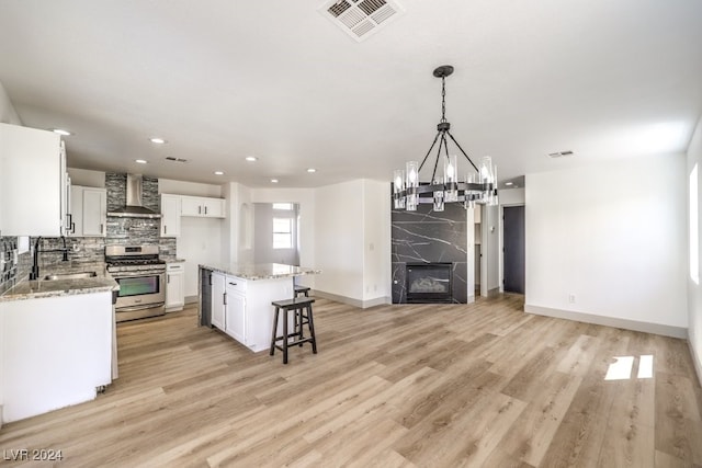 kitchen with wall chimney range hood, gas range, sink, a center island, and white cabinets