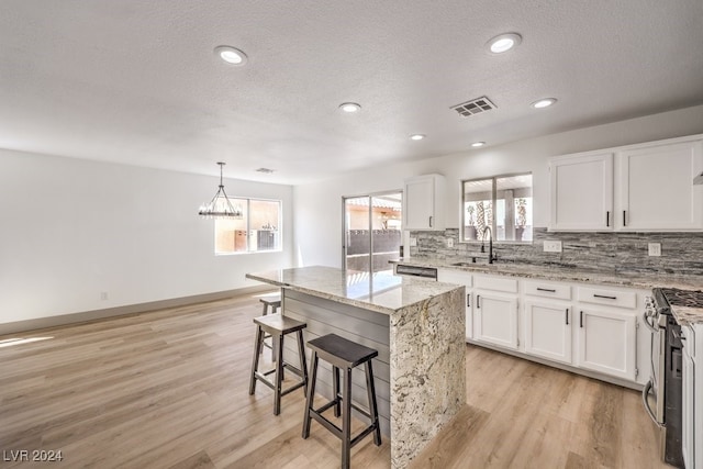 kitchen with an inviting chandelier, white cabinetry, stainless steel appliances, light hardwood / wood-style floors, and a center island