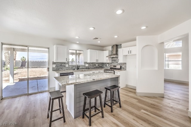 kitchen with a kitchen island, white cabinetry, stainless steel appliances, wall chimney exhaust hood, and light hardwood / wood-style flooring