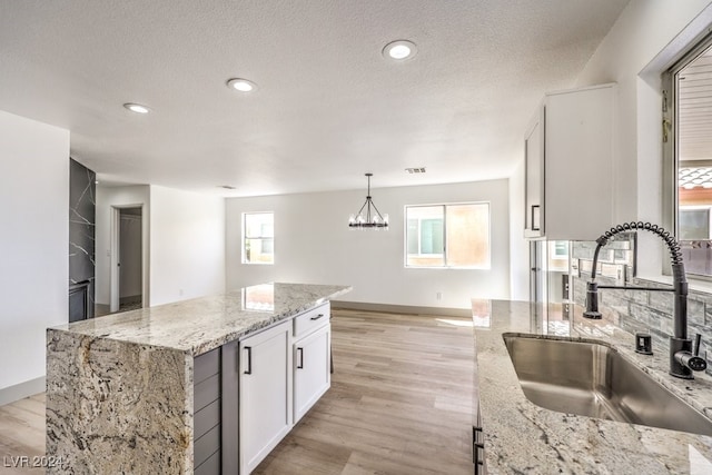 kitchen featuring light stone countertops, sink, a kitchen island, pendant lighting, and white cabinets